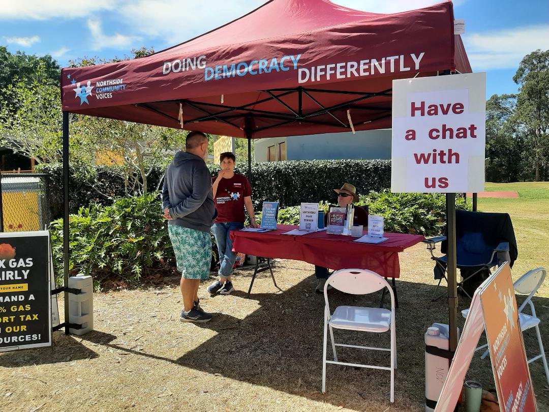 An NCV volunteer talking with a resident at the NCV table under a marquee at Leslie Patrick Park, Arana Hills